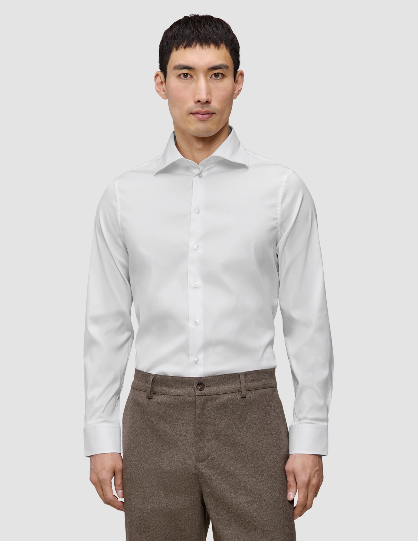 En mann kledd i en Elevated Shirt White Slim i Pima-bomull med spredt krage og brune bukser.